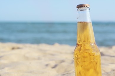 Bottle of cold beer on beach near sea, closeup. Space for text