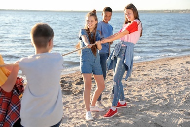 Group of children pulling rope during tug of war game on beach. Summer camp