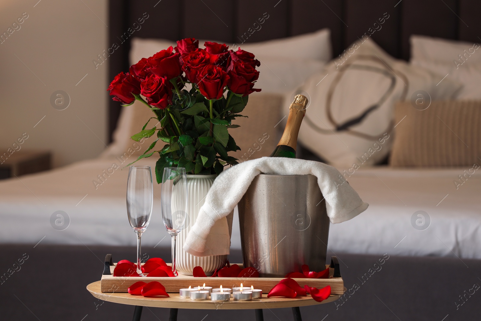 Photo of Honeymoon. Sparkling wine, glasses and bouquet of roses on wooden table in room