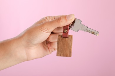 Photo of Woman holding key with wooden keychain on pink background, closeup