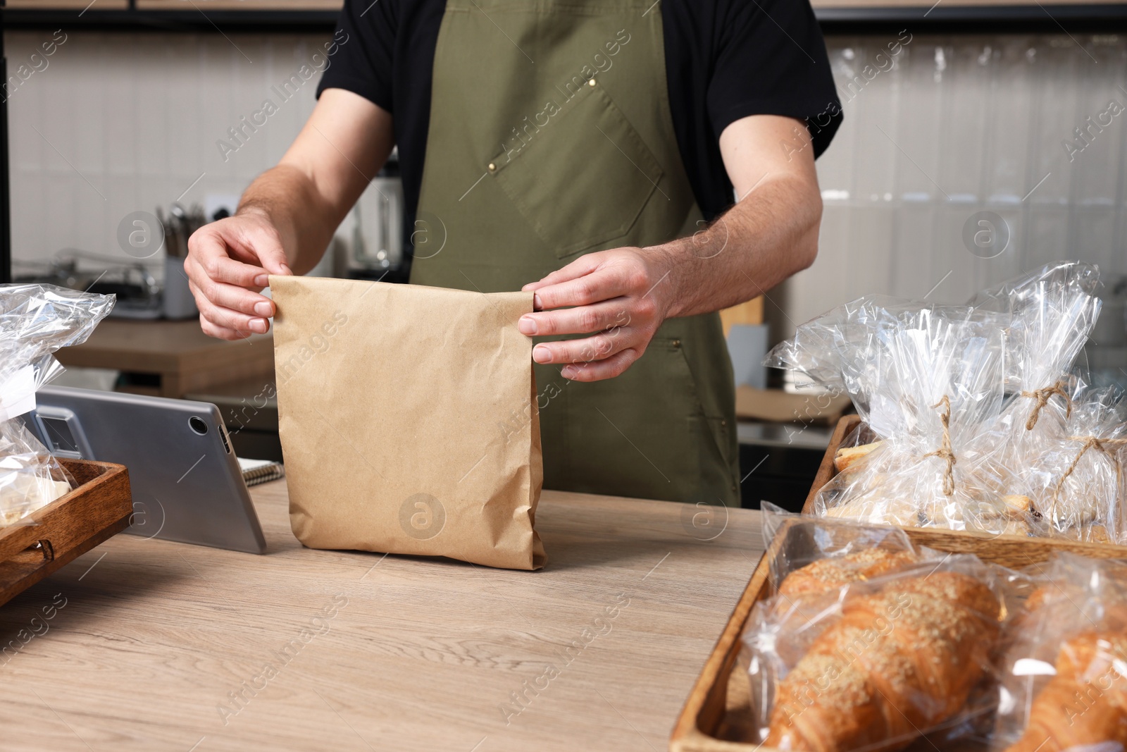 Photo of Seller with paper bag at cashier desk in bakery shop, closeup