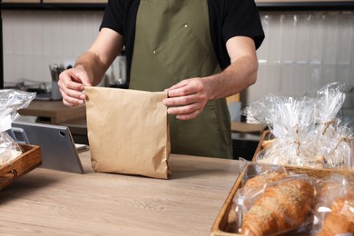 Seller with paper bag at cashier desk in bakery shop, closeup