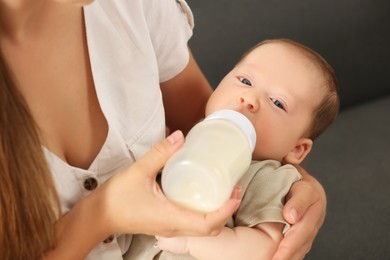 Mother feeding her cute child with infant formula indoors