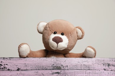 Photo of Cute teddy bear behind pink wooden table against light grey background