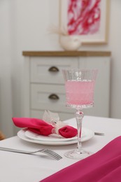 Photo of Table setting. Glass of tasty beverage, plates with pink napkin and cutlery in dining room