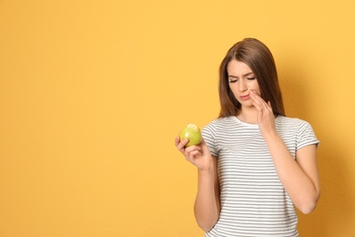 Photo of Emotional young woman with sensitive teeth and apple on color background. Space for text