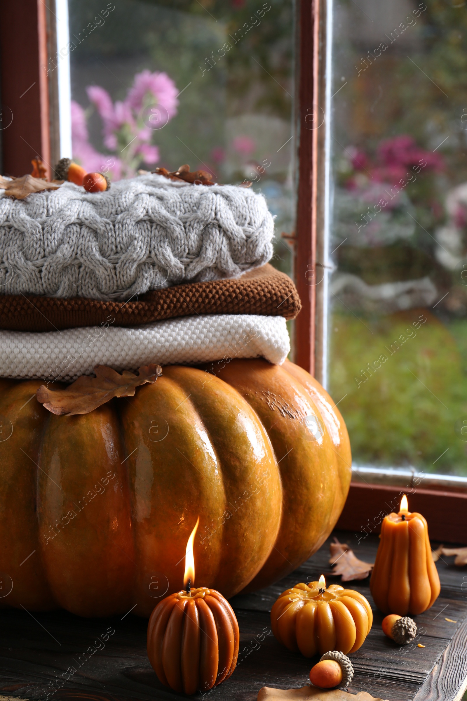 Photo of Beautiful burning candles in shape of pumpkins on wooden table near window. Autumn atmosphere