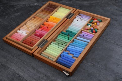 Photo of Set of colorful pastels in wooden box on grey stone table. Drawing materials
