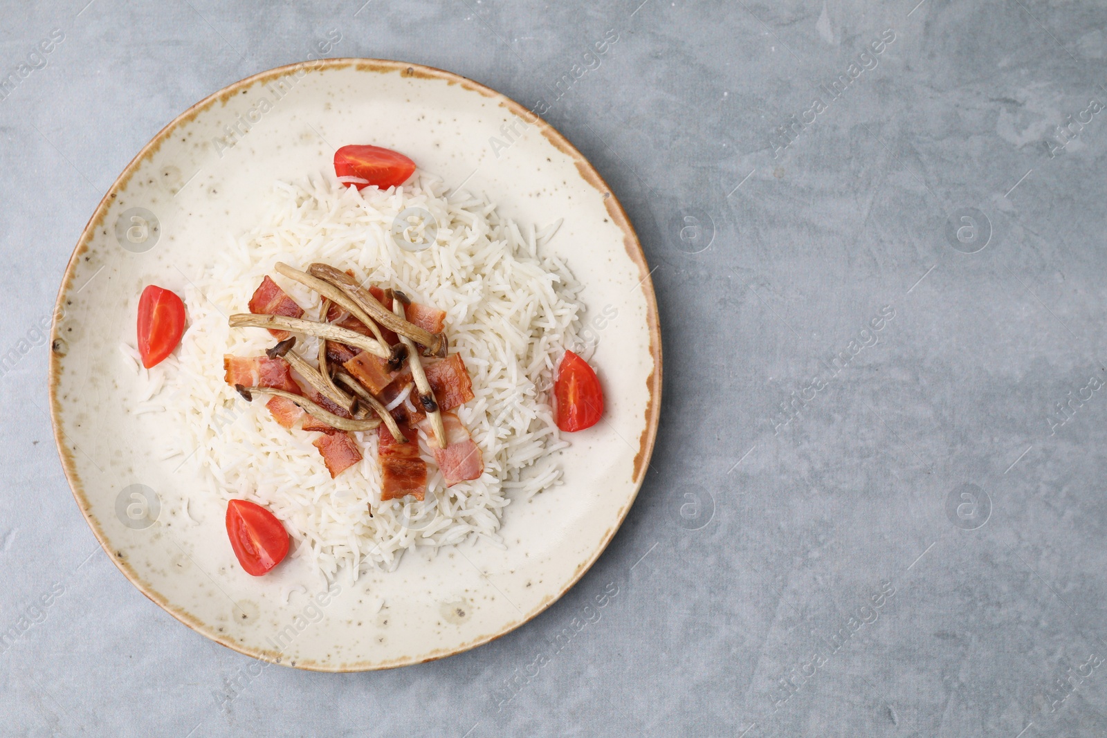 Photo of Delicious rice with bacon, mushrooms and tomatoes on gray table, top view. Space for text