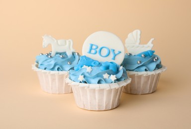 Delicious cupcakes with light blue cream and toppers for baby shower on beige background