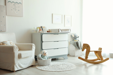 Photo of Beautiful baby room interior with toys, armchair and modern changing table