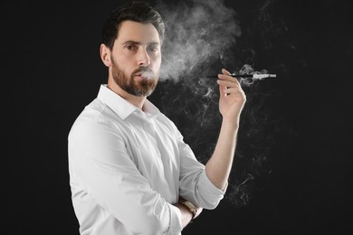 Photo of Man using long cigarette holder for smoking on black background, space for text