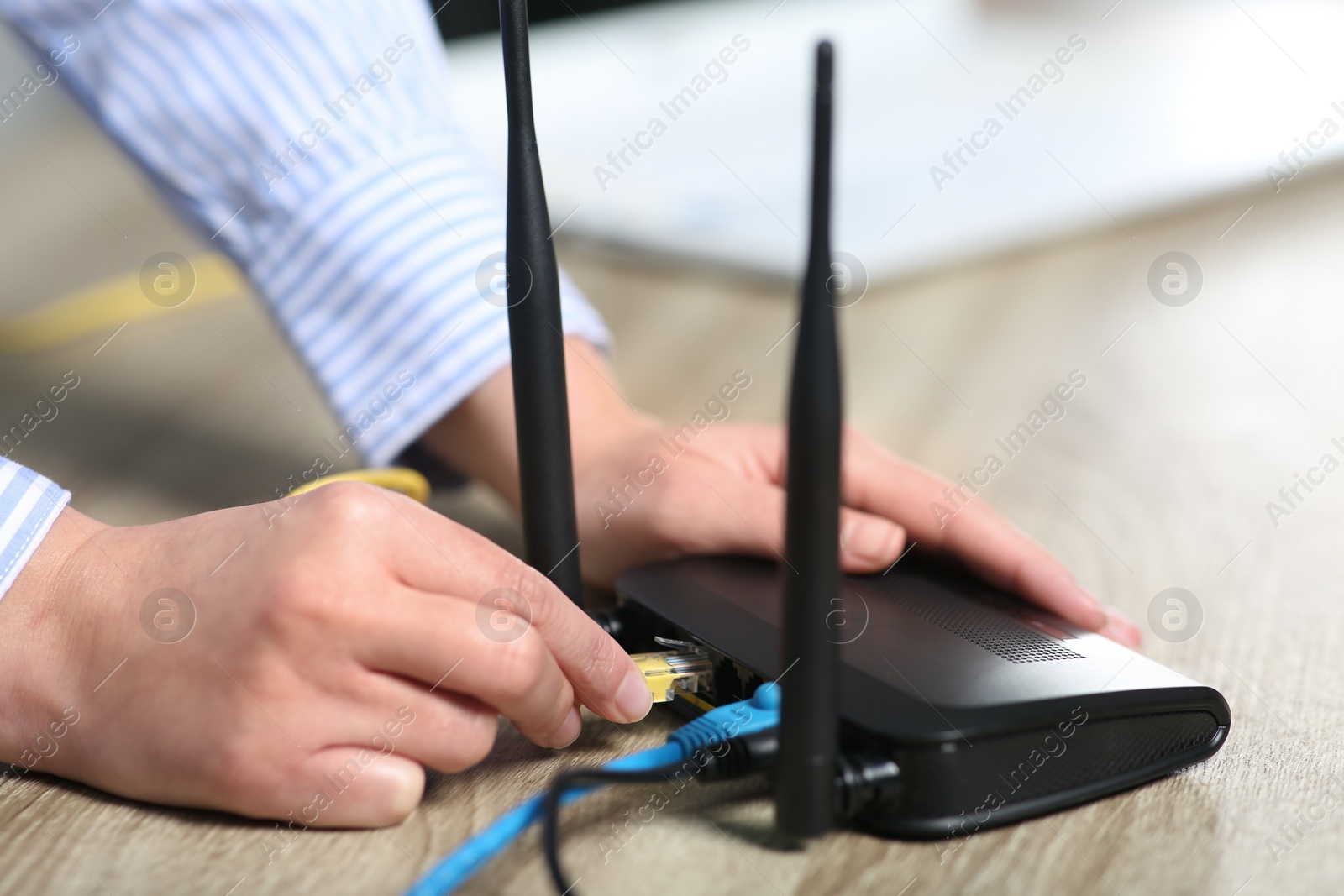 Photo of Woman inserting ethernet cable into Wi-Fi router at table indoors, closeup