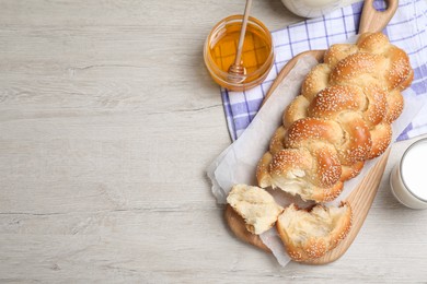 Photo of Broken homemade braided bread, milk with honey on white wooden table, flat lay and space for text. Traditional Shabbat challah