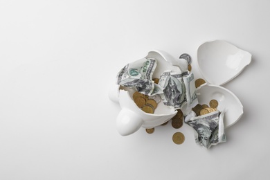 Broken piggy bank with coins and banknotes on white background