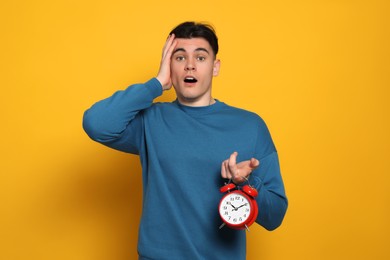 Photo of Emotional young man with alarm clock on orange background. Being late concept
