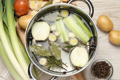 Pot and different ingredients for cooking tasty bouillon on white wooden table, flat lay