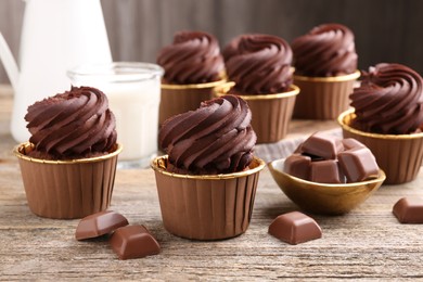 Photo of Delicious cupcakes and chocolate pieces on wooden table