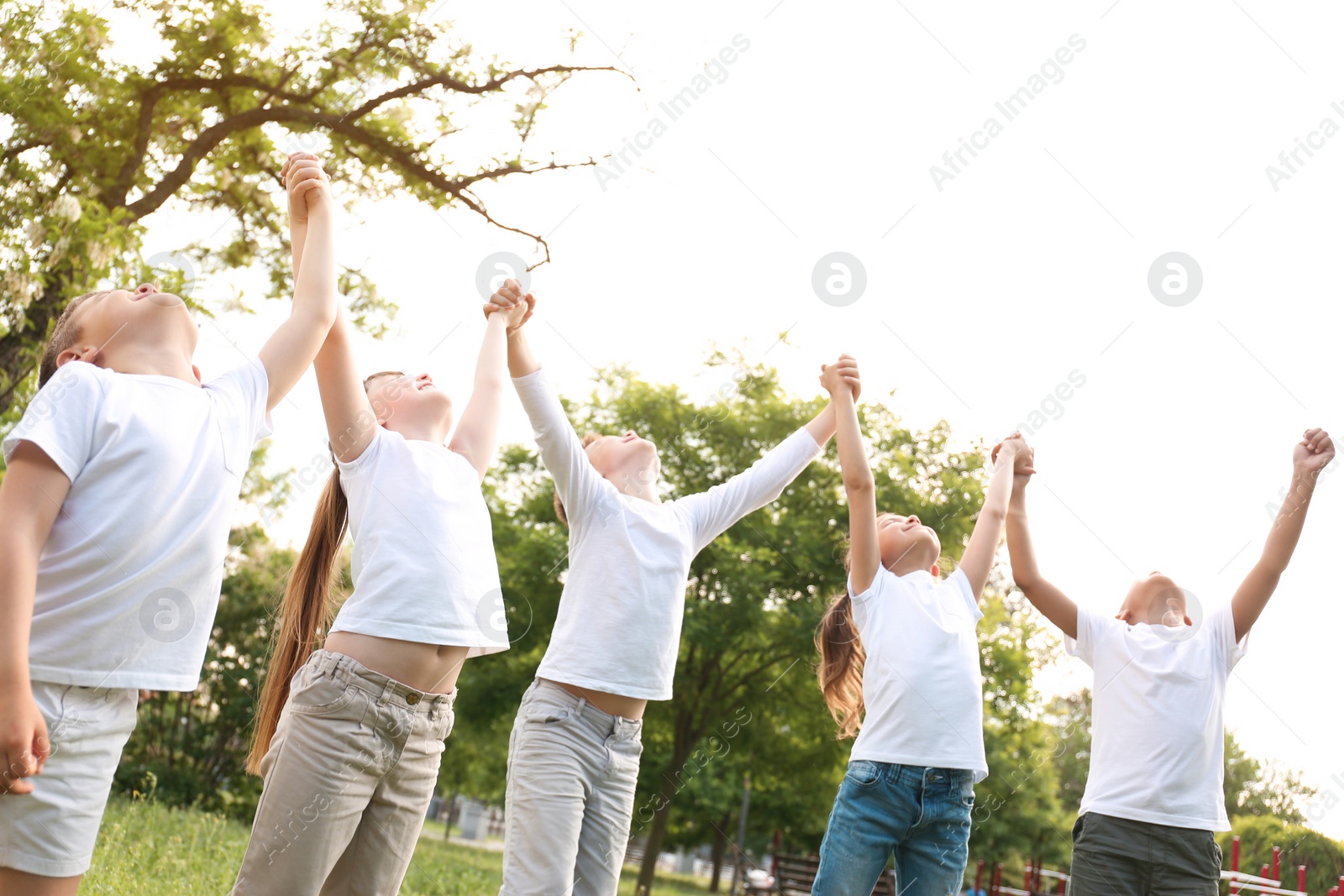 Photo of Group of children holding hands up in park. Volunteer project