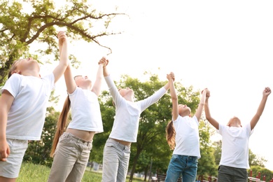 Group of children holding hands up in park. Volunteer project