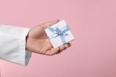 Photo of Doctor holding gift box on pink background, closeup. Medical present