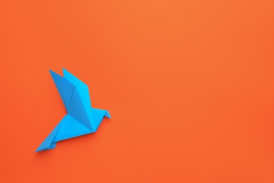 Photo of Beautiful light blue origami bird on orange background, top view. Space for text