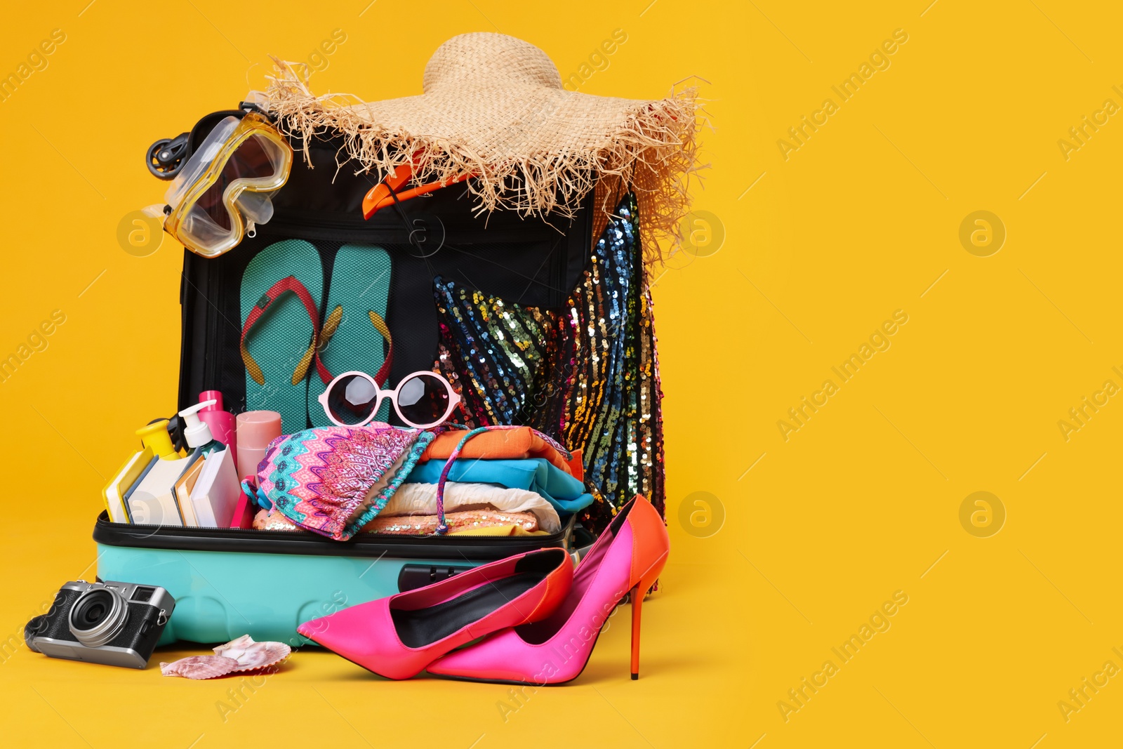 Photo of Open suitcase with clothes, beach accessories and shoes on yellow background, space for text. Summer vacation