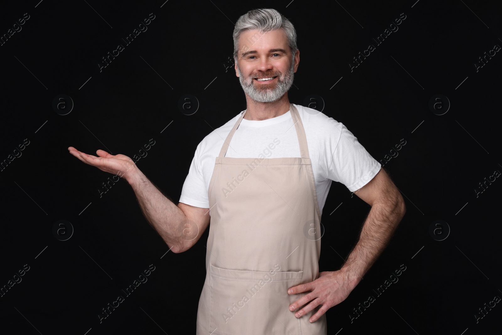 Photo of Happy man wearing kitchen apron on black background. Mockup for design