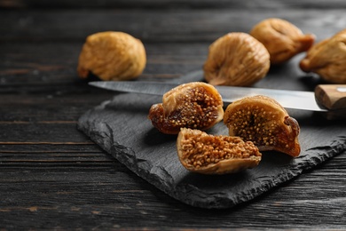 Photo of Slate plate with tasty dried figs on black wooden table, closeup. Space for text