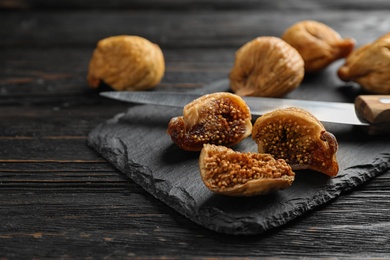 Slate plate with tasty dried figs on black wooden table, closeup. Space for text