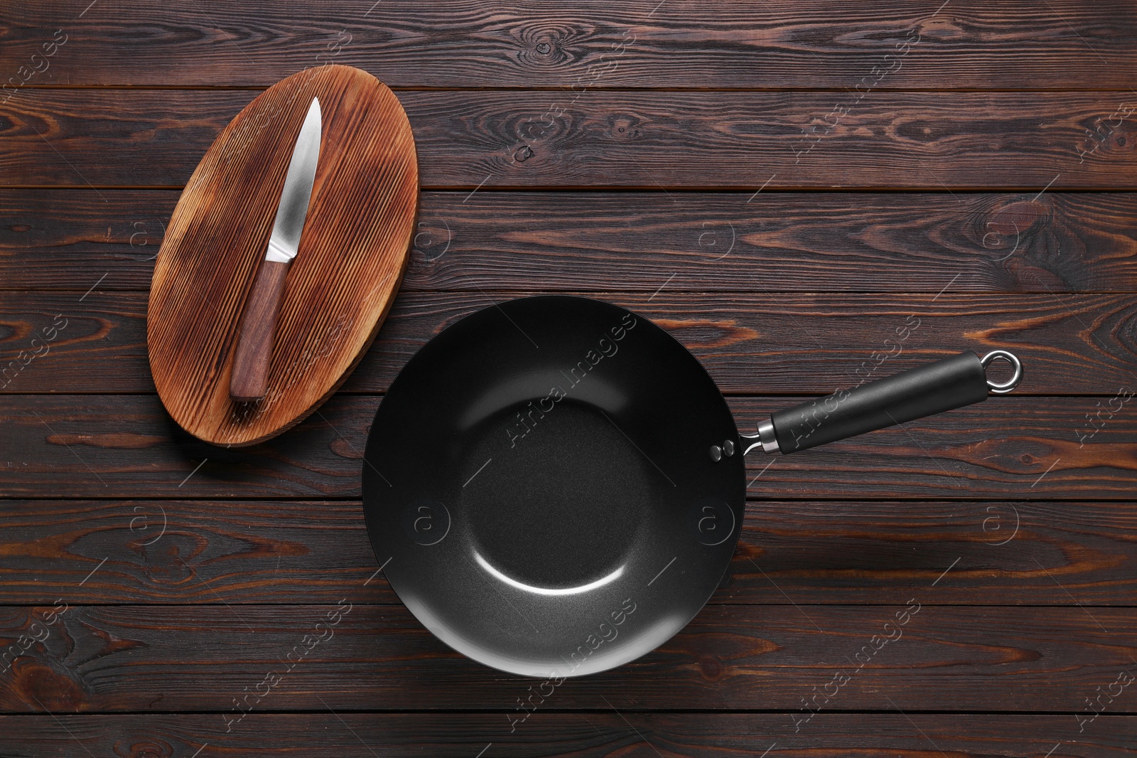 Photo of Empty iron wok, knife and cutting board on wooden table, flat lay