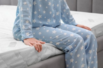 Photo of Woman sitting on new soft mattress indoors, closeup