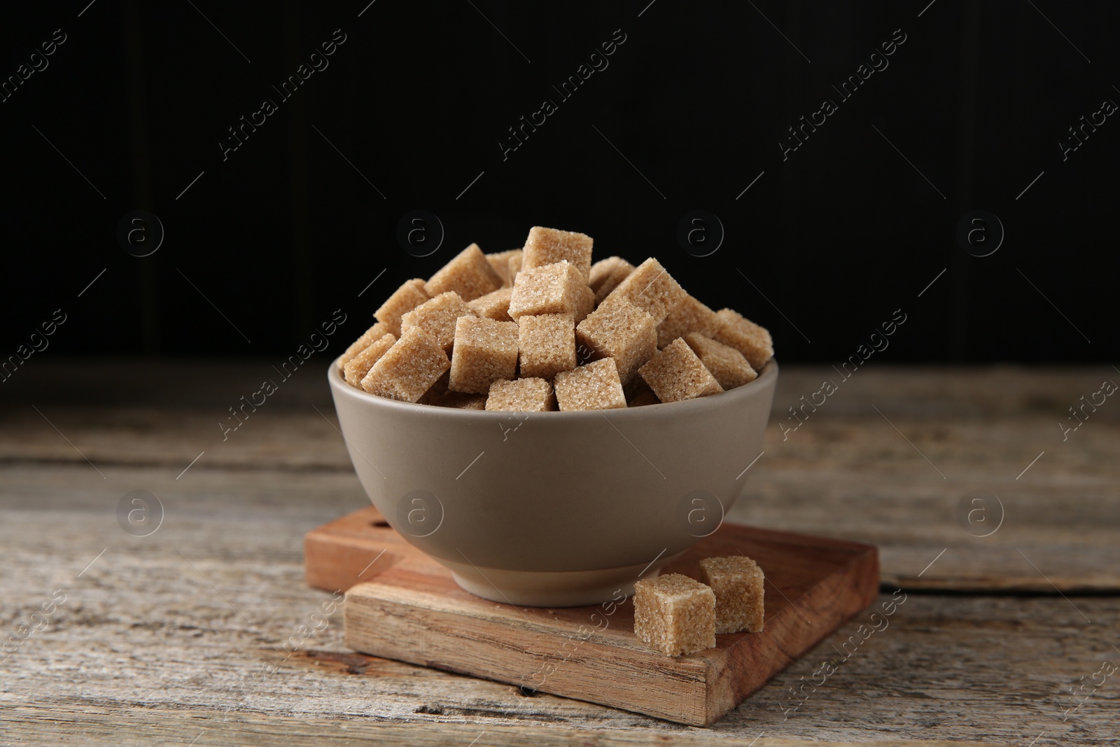 Photo of Bowl with brown sugar cubes on wooden table