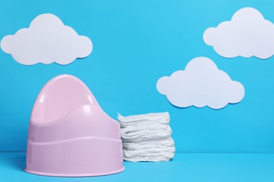 Photo of Pink baby potty and stack of diapers against light blue background with paper clouds, space for text. Toilet training