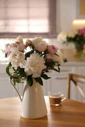 Photo of Beautiful peonies and cup of coffee on wooden table in kitchen