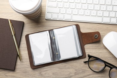 Photo of Leather business card holder with blank cards, stationery and keyboard on wooden table, flat lay
