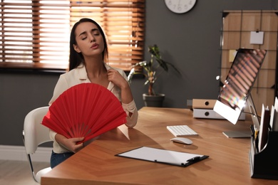 Woman with hand fan suffering from heat at home. Summer season