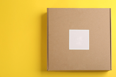 Photo of Closed cardboard box on yellow background, top view. Space for text