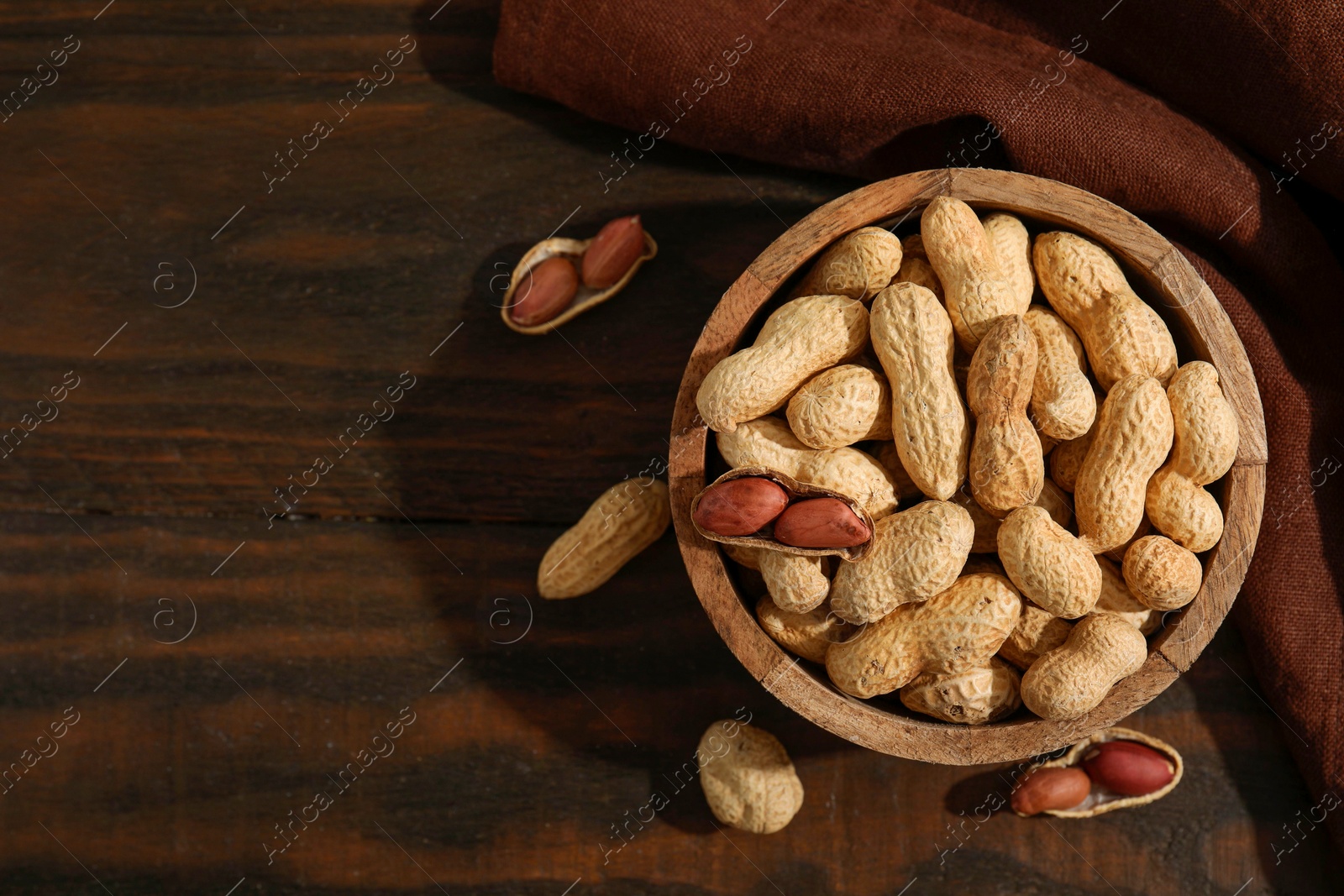 Photo of Fresh unpeeled peanuts in bowl on wooden table, top view. Space for text