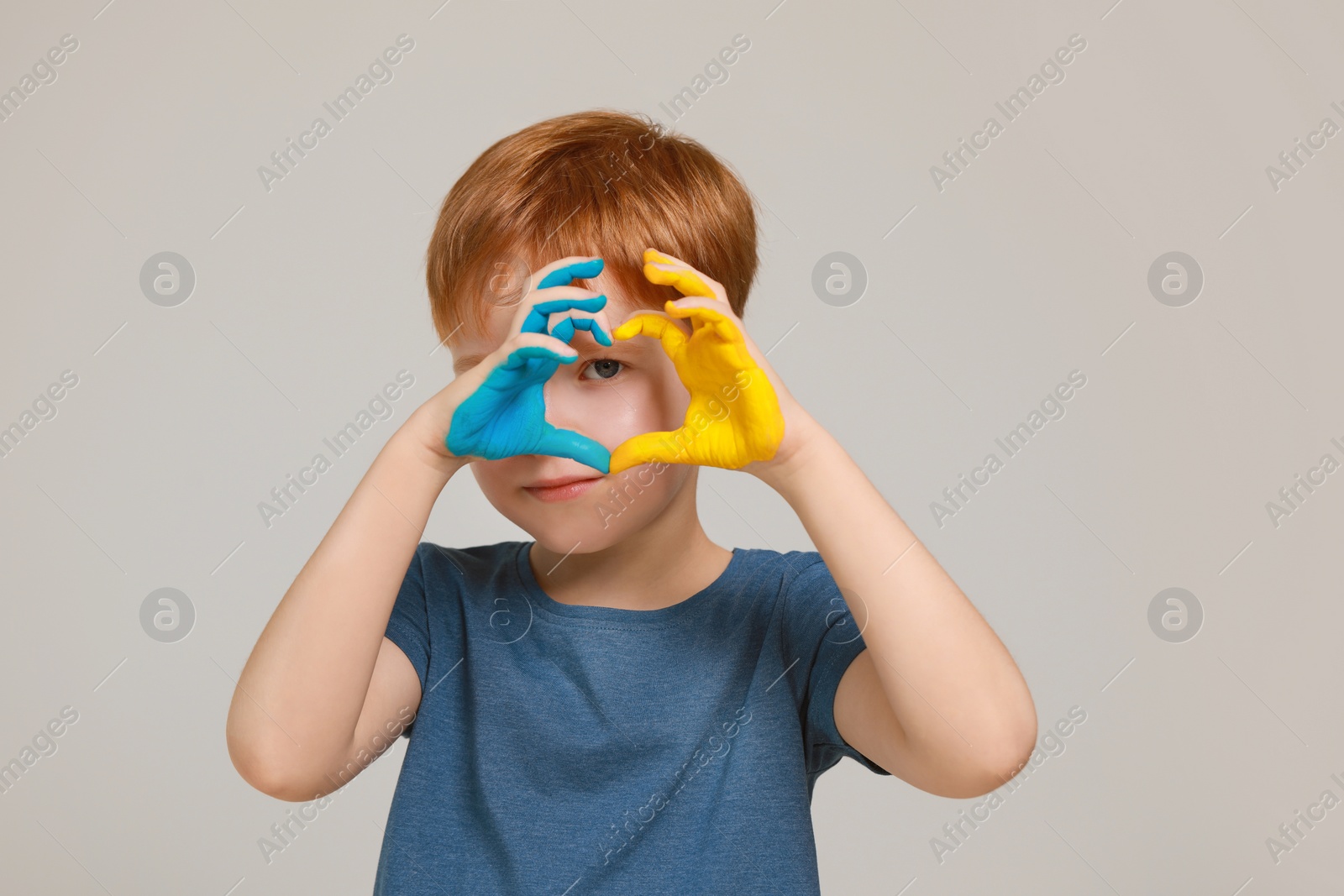 Photo of Little boy making heart with his hands painted in Ukrainian flag colors on light grey background. Love Ukraine concept