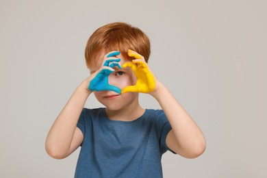 Photo of Little boy making heart with his hands painted in Ukrainian flag colors on light grey background. Love Ukraine concept