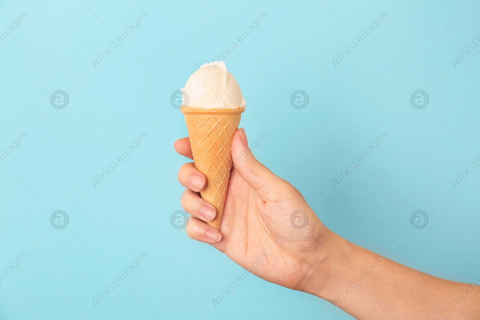 Photo of Woman holding waffle cone with tasty vanilla ice cream on color background