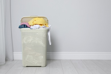 Photo of Plastic laundry basket full of dirty clothes on floor near light wall. Space for text