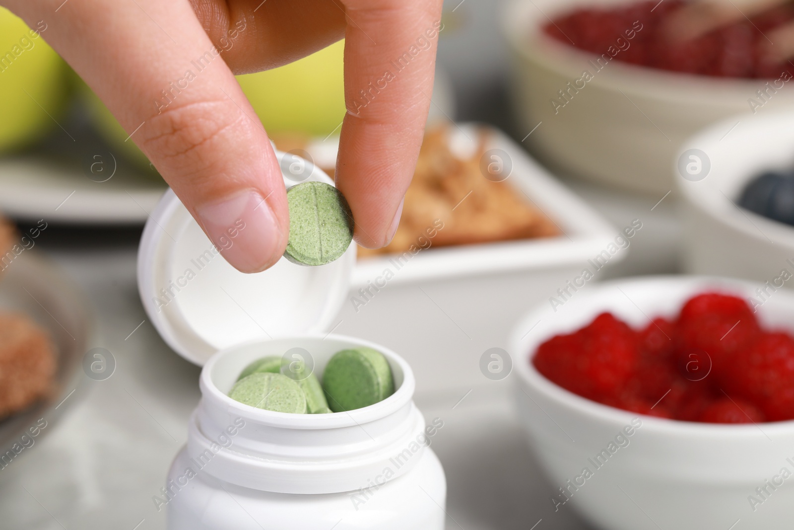 Photo of Woman taking pill from bottle at table, closeup. Prebiotic supplements
