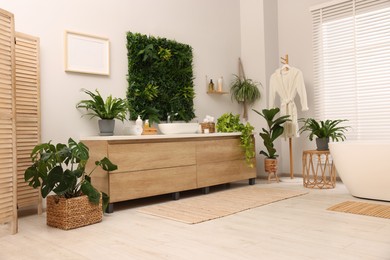 Green artificial plants, vanity and different personal care products in bathroom