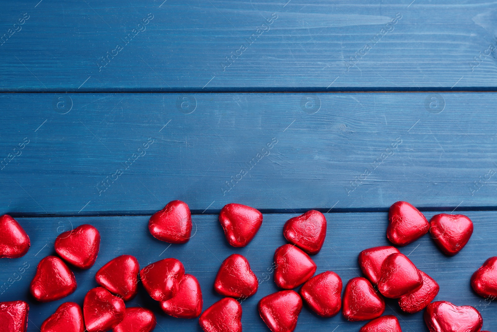 Photo of Heart shaped chocolate candies on blue wooden table, flat lay. Space for text