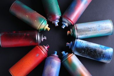 Many spray paint cans on black background, top view