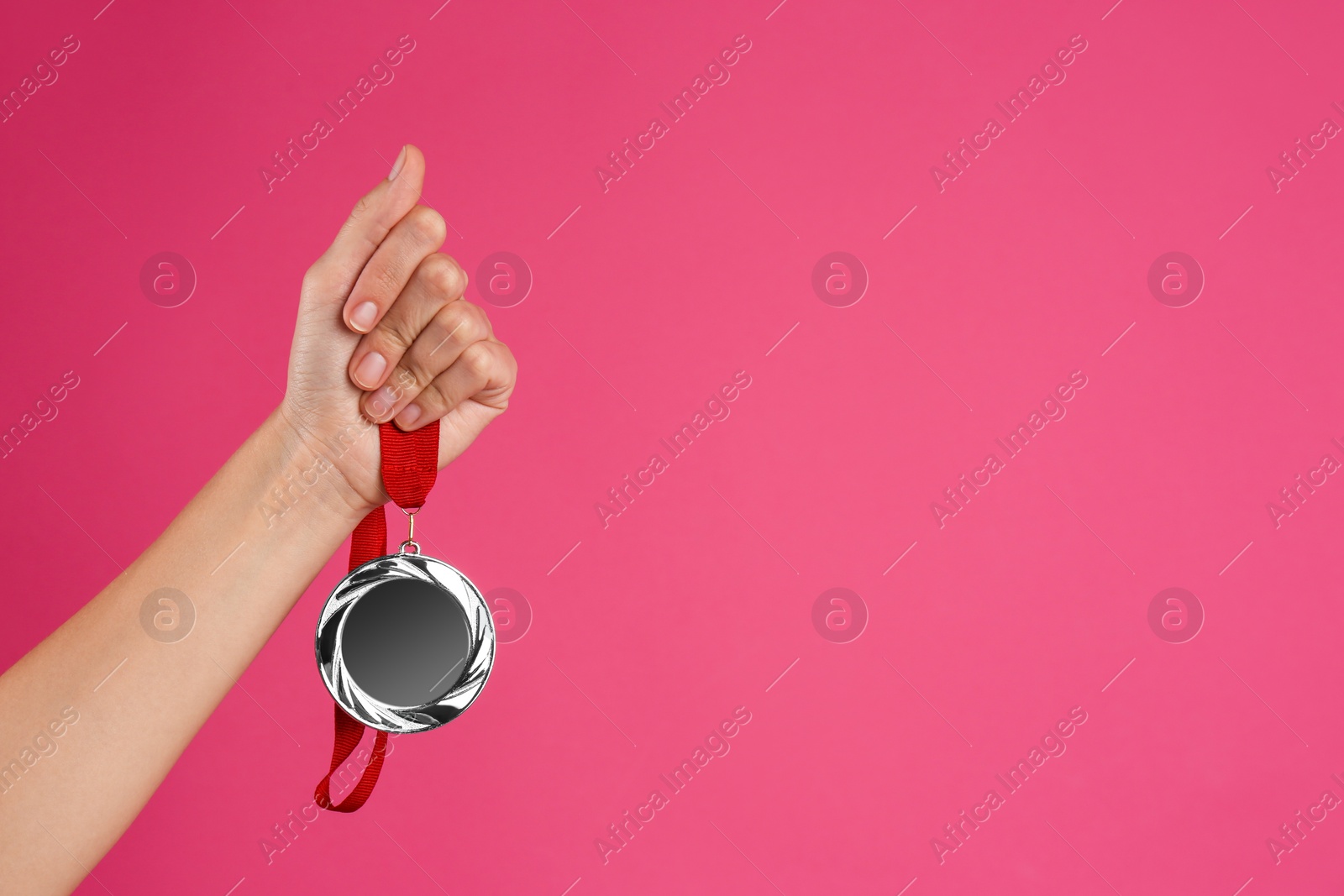 Photo of Woman holding silver medal on pink background, closeup. Space for design