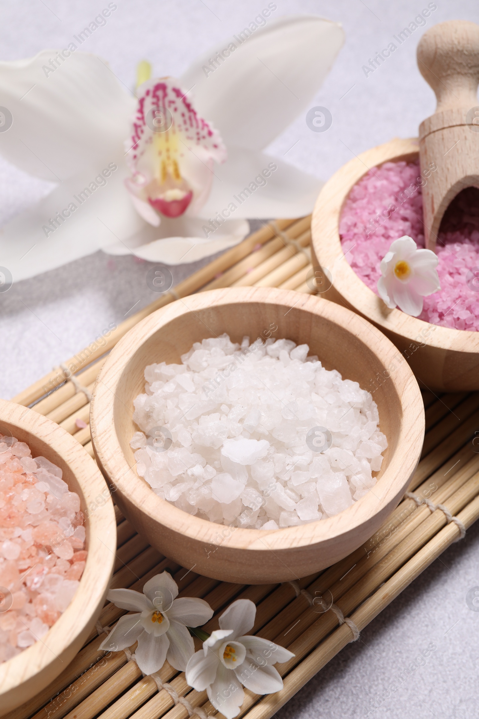 Photo of Different types of sea salt and flowers on light table, closeup. Spa products