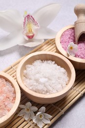 Photo of Different types of sea salt and flowers on light table, closeup. Spa products